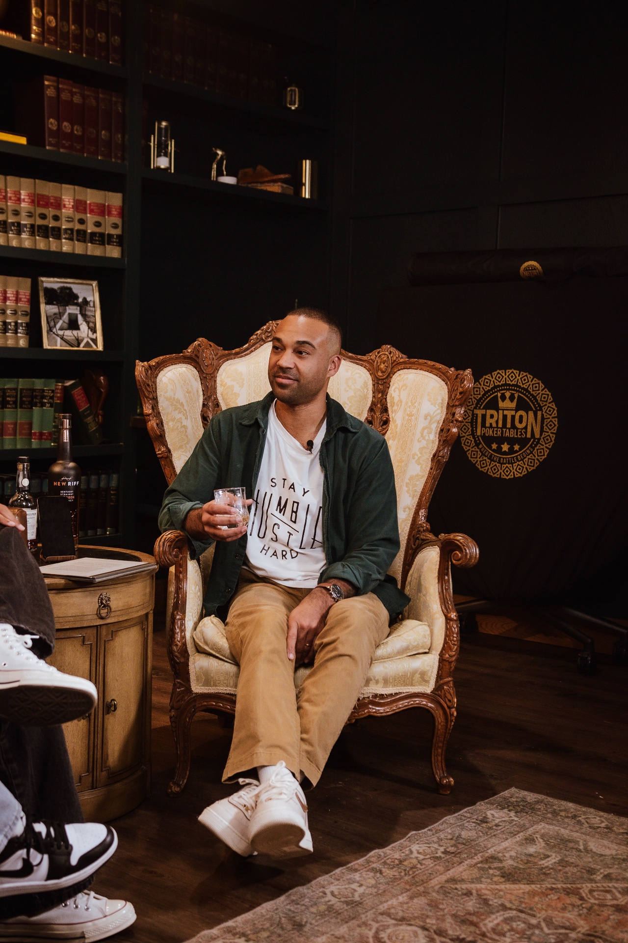 Host Arian Green seated in the carved armchair at The Fort with a glass of bourbon during a taping of AI on the Rocks