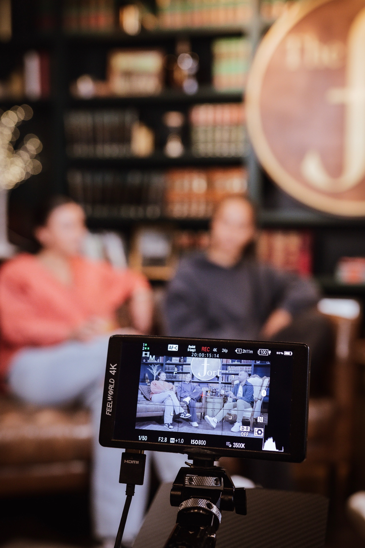 A 4K monitor framing two guests mid-taping, the Fort sign glowing behind them