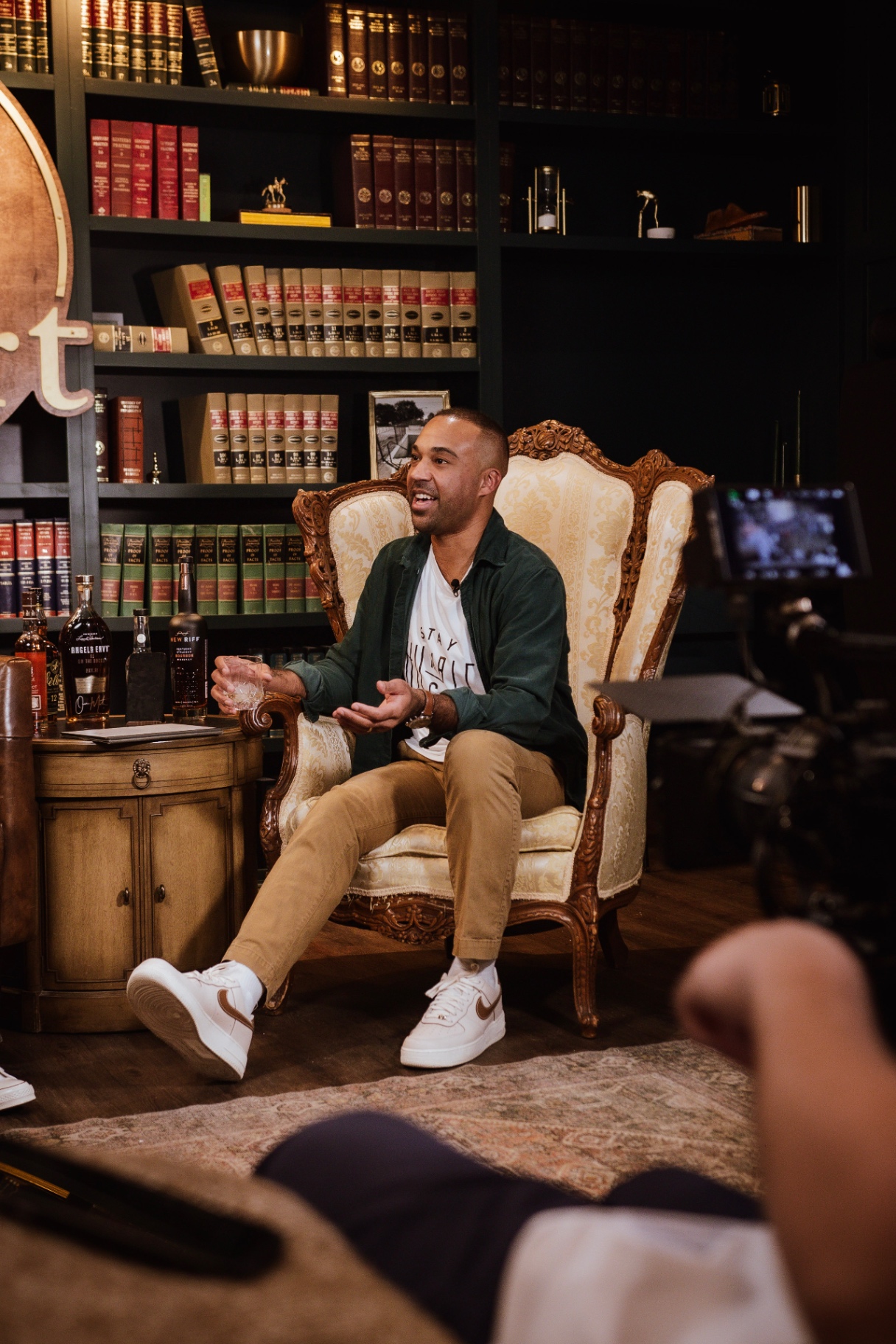 Host Arian Green mid-conversation on the set of AI on the Rocks, the production monitor visible in frame