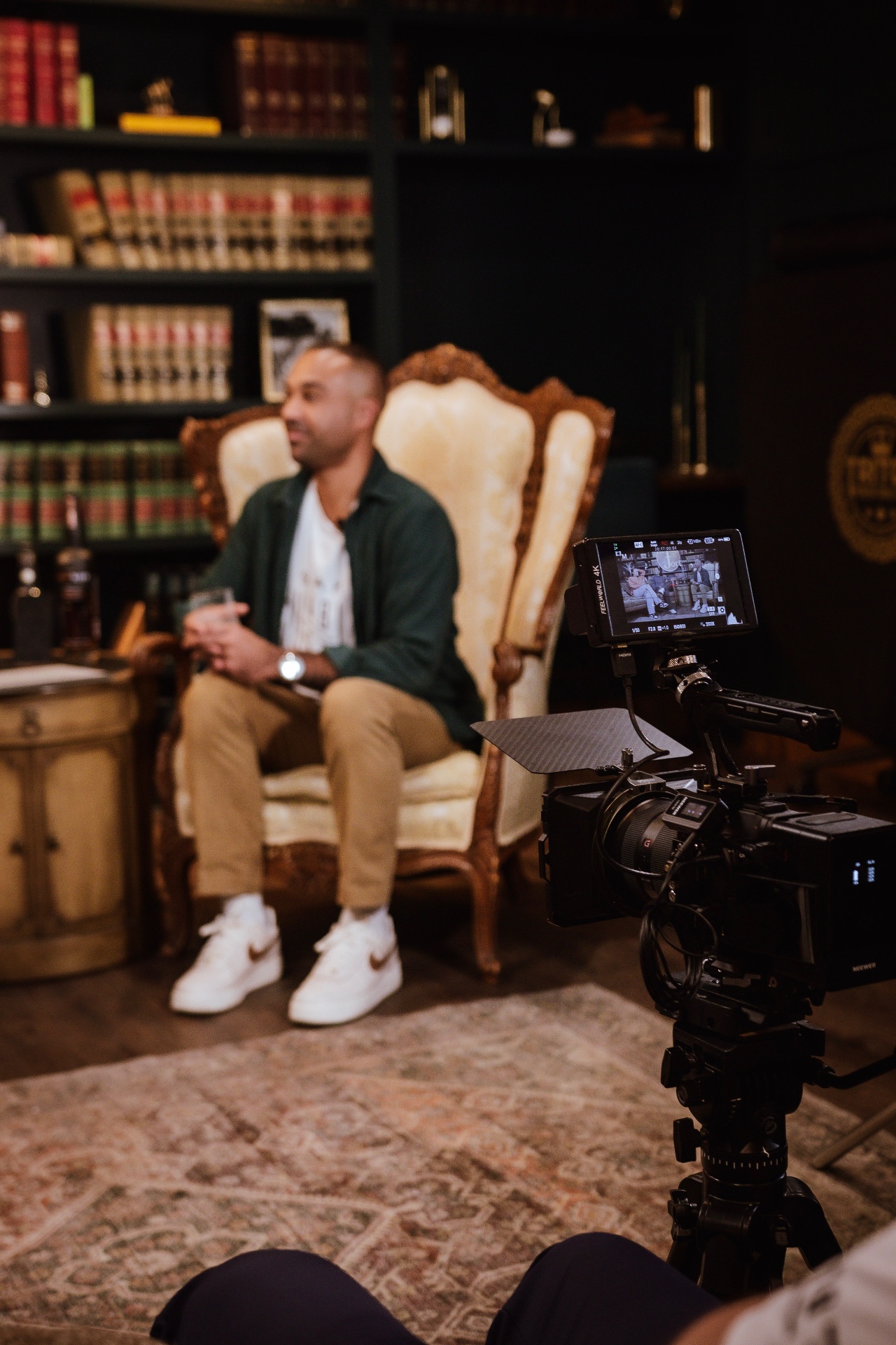 The AI on the Rocks set at The Fort — a guest in a carved armchair, bourbon bottles on the side table, and the full camera rig in frame
